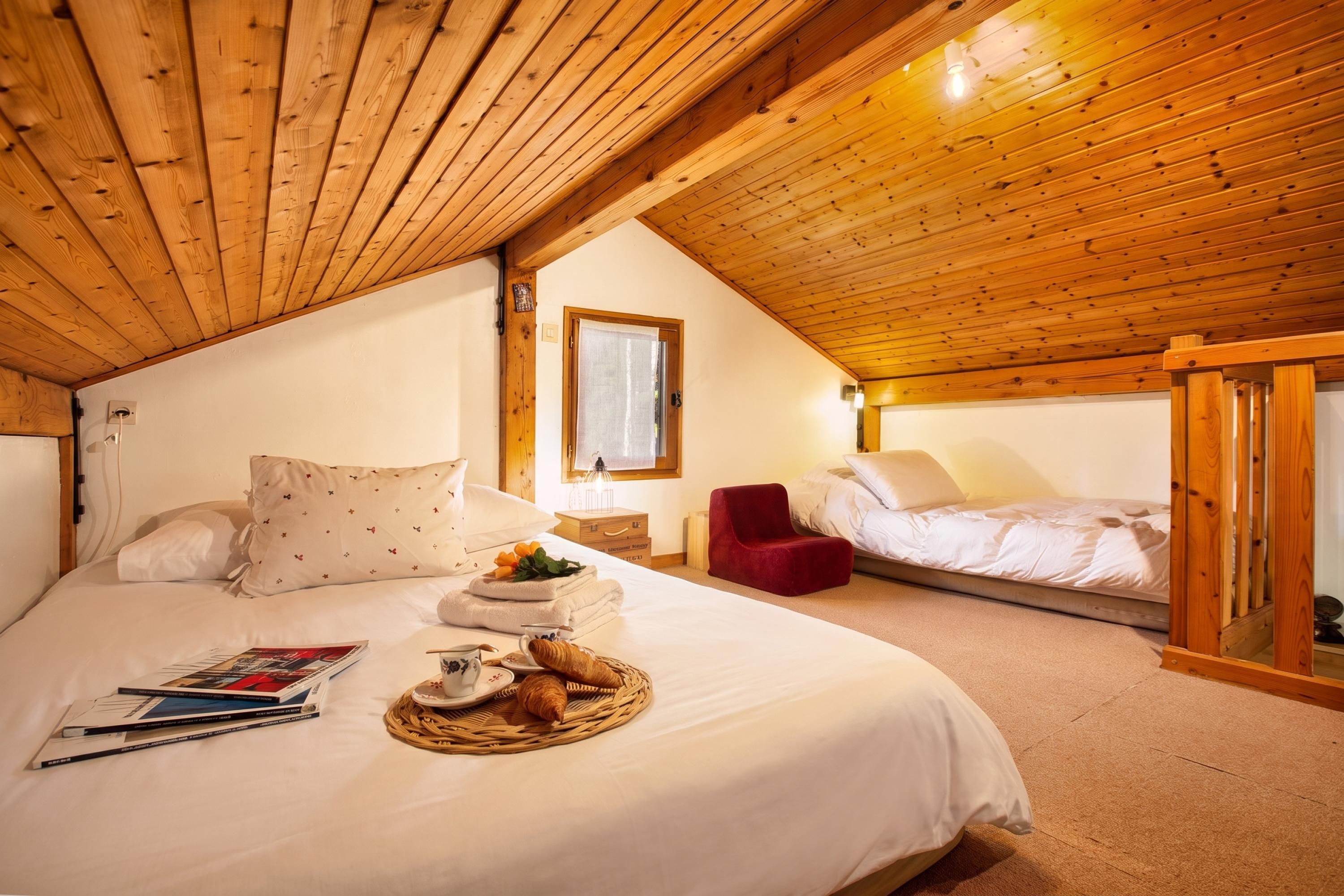 Een gezellige slaapkamer met een houten plafond, een bed met wit beddengoed, een rode stoel en een klein tafeltje met ontbijtartikelen.