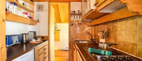 Cocina compacta con armarios de madera, un microondas integrado, estufa y pileta.