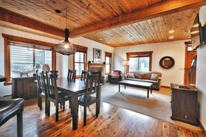 Una sala de estar amplia con techo de madera, un comedor con mesa y sillas grandes, y una zona de estar acogedora con sofá y chimenea.