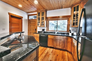 Une cuisine avec des meubles de rangement en bois, un réfrigérateur noir et une fenêtre donnant sur une maison.