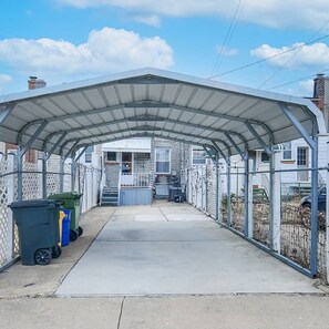 A covered outdoor area with a concrete pathway, metal fencing, and a row of trash bins.