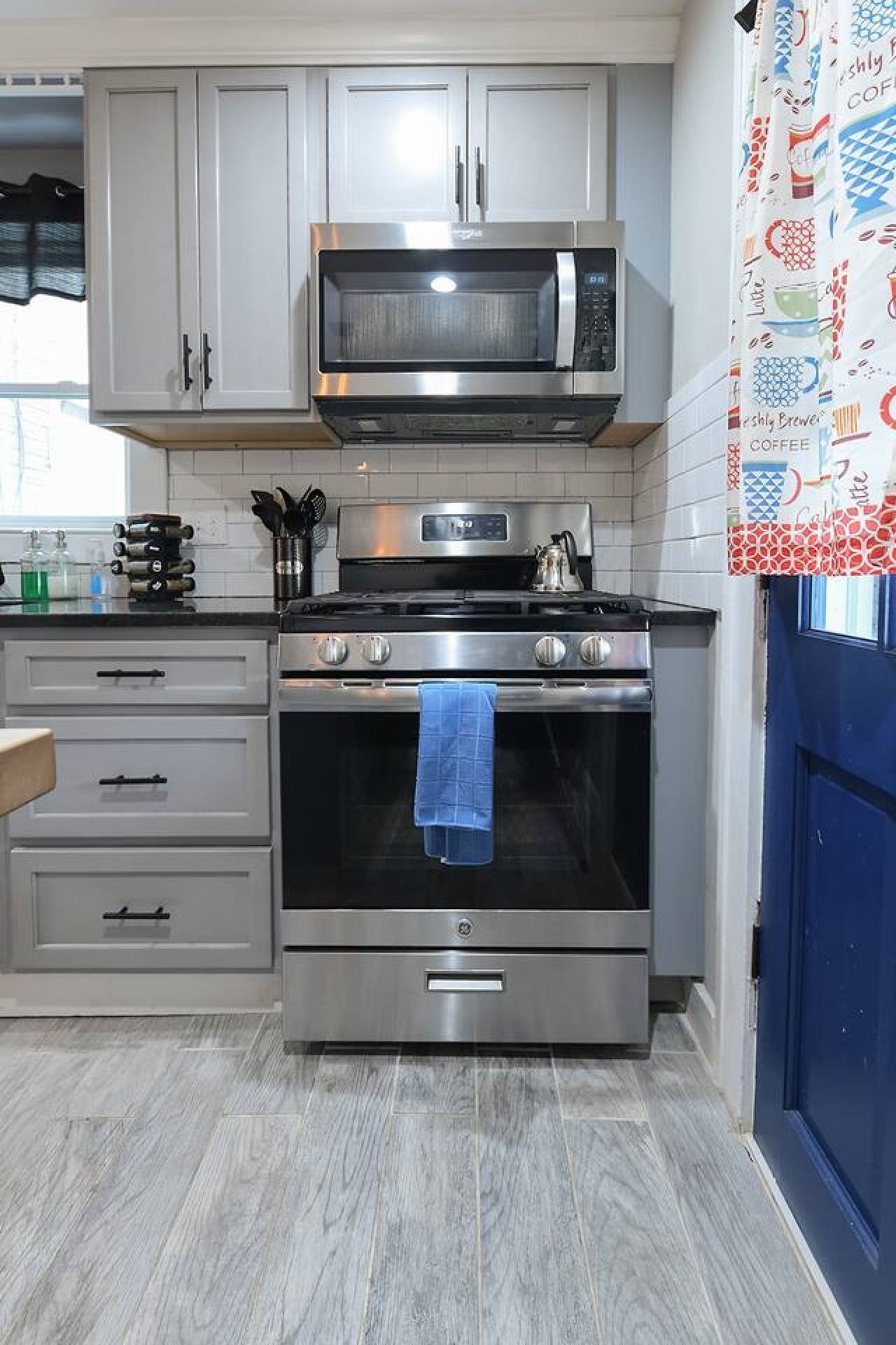 A kitchen with stainless steel appliances, including a microwave and oven, and a blue towel hanging inside the oven.