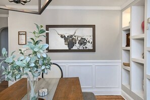 A dining area with a wooden table, a framed artwork of a bull's head, and a potted plant.