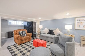 A living room with a patterned sofa, a grey sofa, a red ottoman, and a checkered rug.