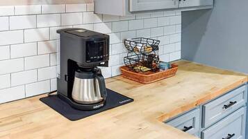 A kitchen with a coffee maker, hanging pendant lights, and white cabinets.