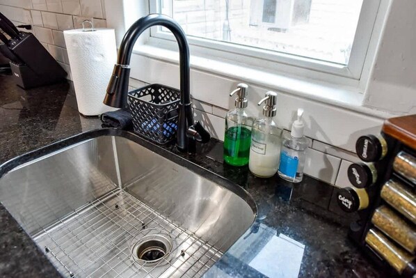A stainless steel kitchen sink with a black faucet, a paper towel holder, and a window above.