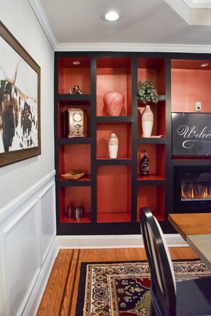 Una habitación con chimenea, una mesa de comedor y un estante rojo con varios objetos decorativos.