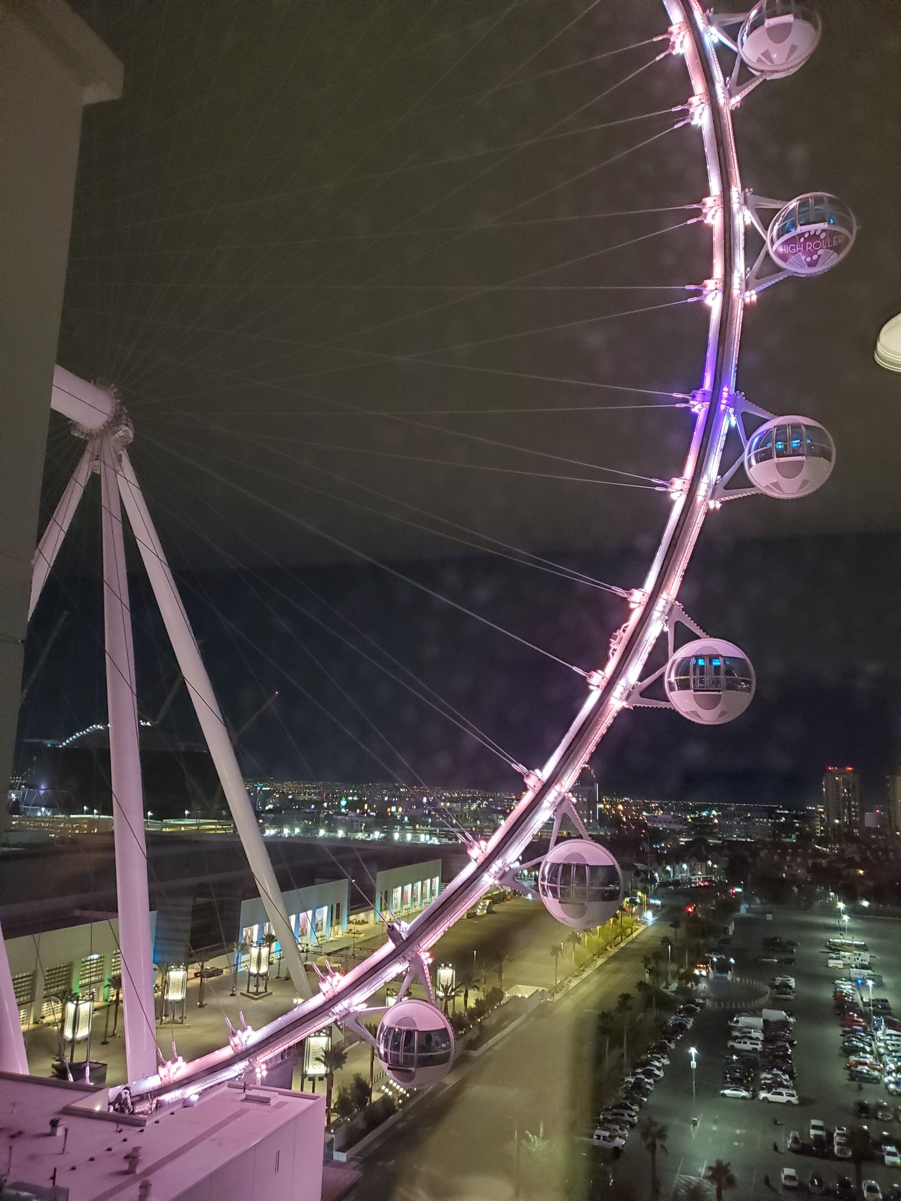 A nighttime view of a large Ferris wheel with gondolas, surrounded by city lights and buildings.