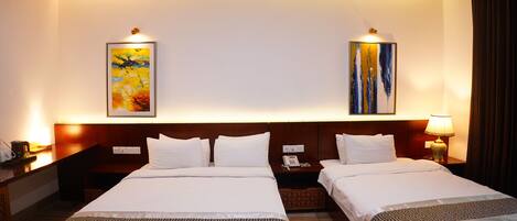 A hotel room with two beds, a wooden headboard, a nightstand with a lamp, and artwork on the walls.
