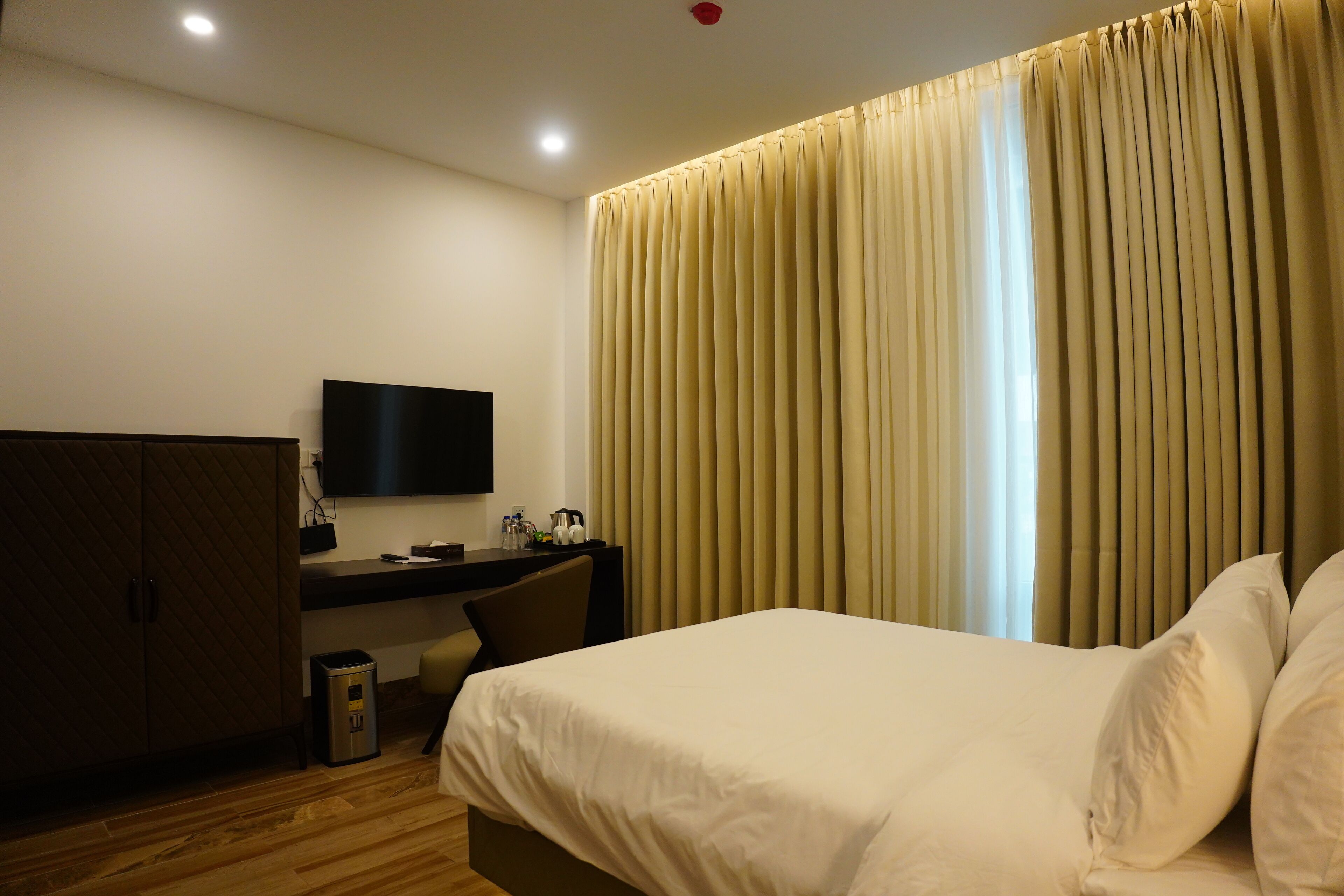 Una habitación de hotel con cama, escritorio, televisión y cortinas.