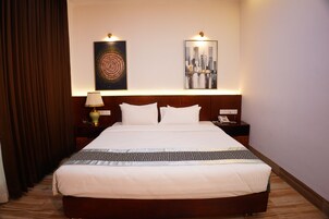 Habitación de hotel con una cama grande, dos mesitas de noche, una lámpara y dos obras de arte colgadas en la pared.