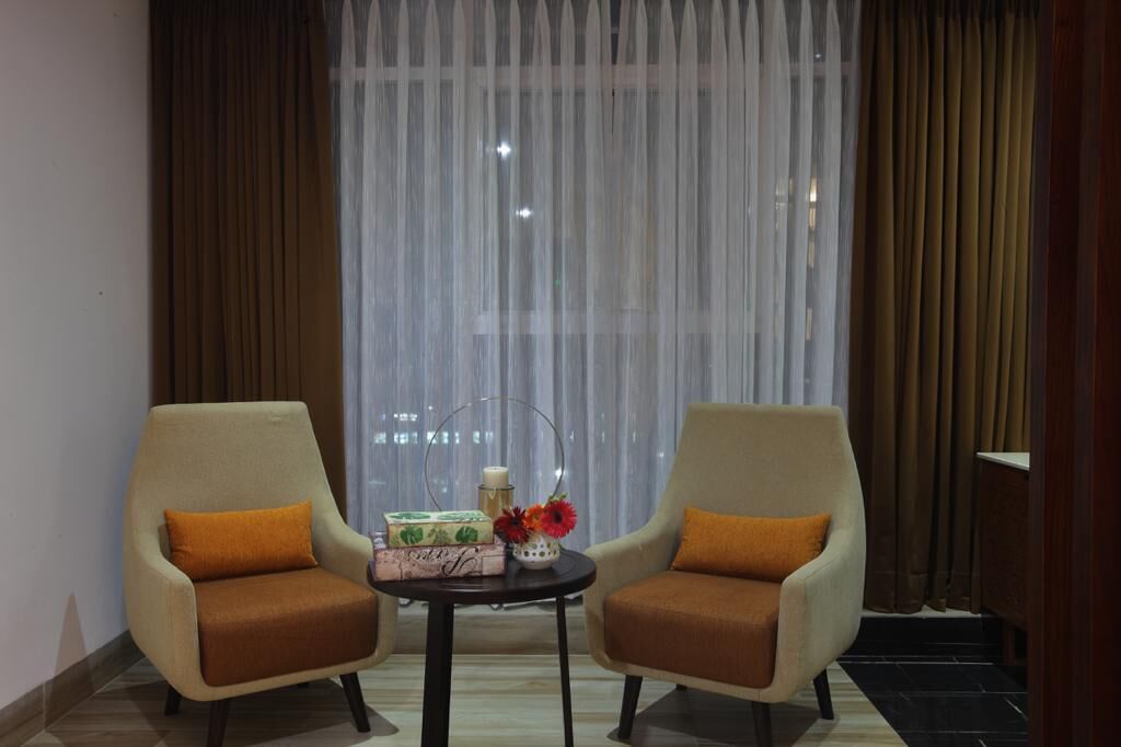 Una habitación con dos sillones, una mesita y un ventanal con cortinas traslúcidas.