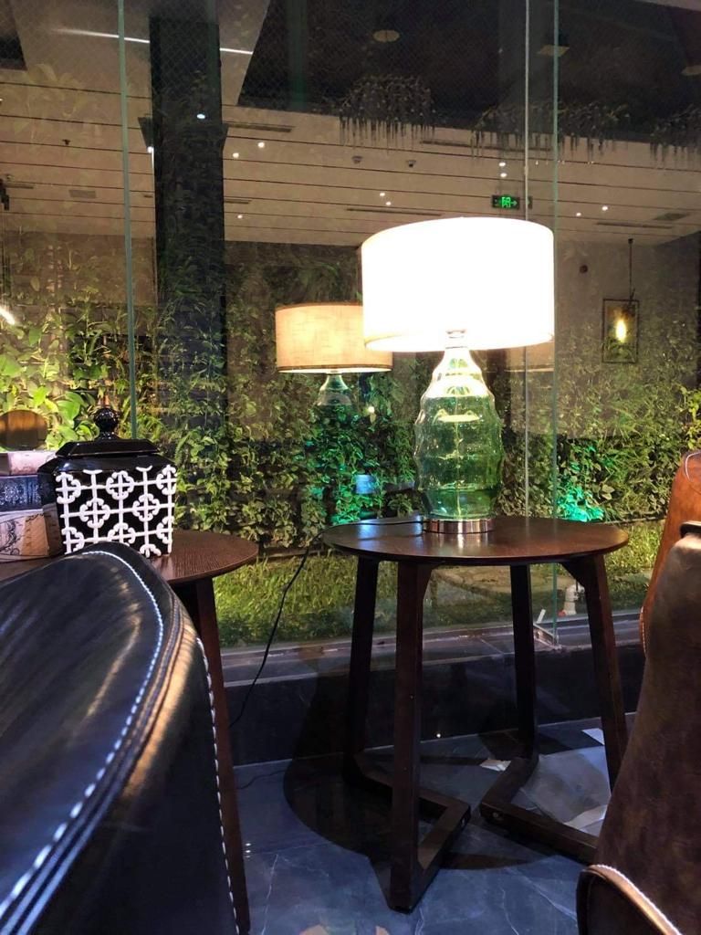 Um interior moderno com divisória de vidro, uma mesa redonda com abajur e uma poltrona de couro.