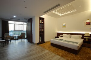 Habitación de hotel con una cama grande, un escritorio, sillas, una estantería y vistas al exterior.