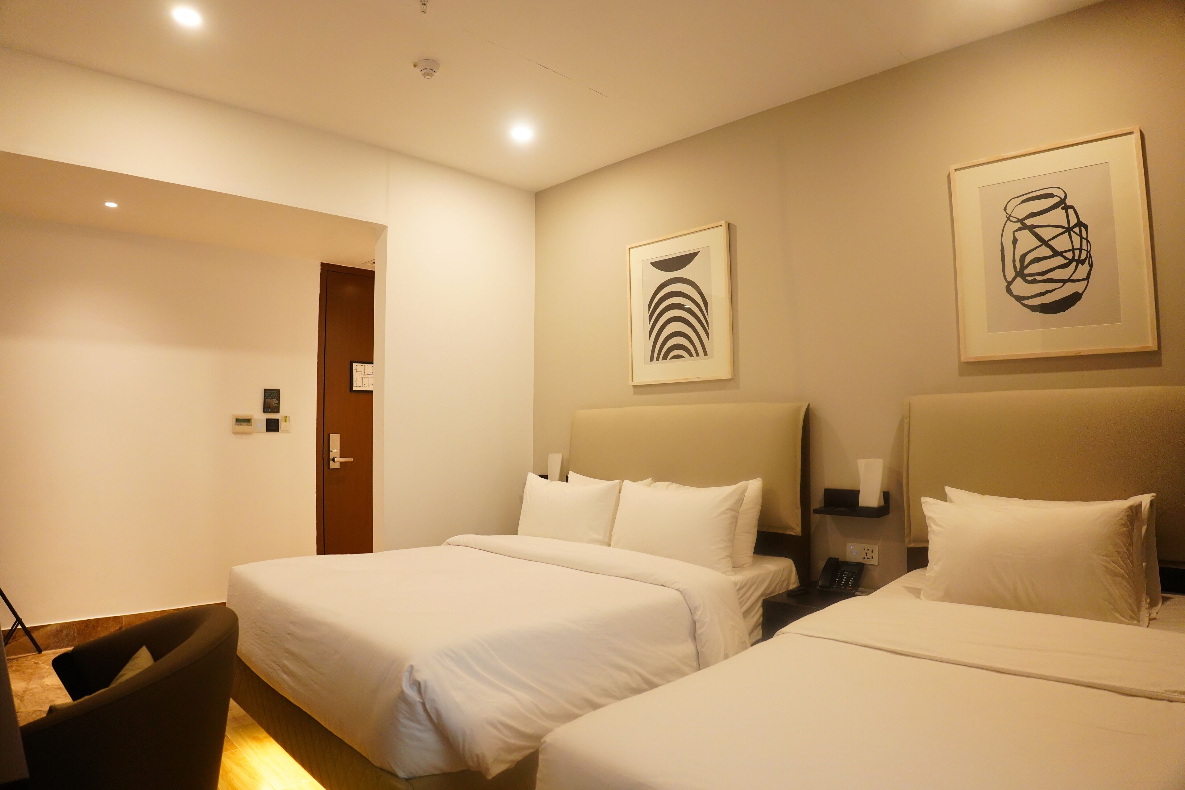 A hotel room with two beds, a chair, and artwork on the walls.