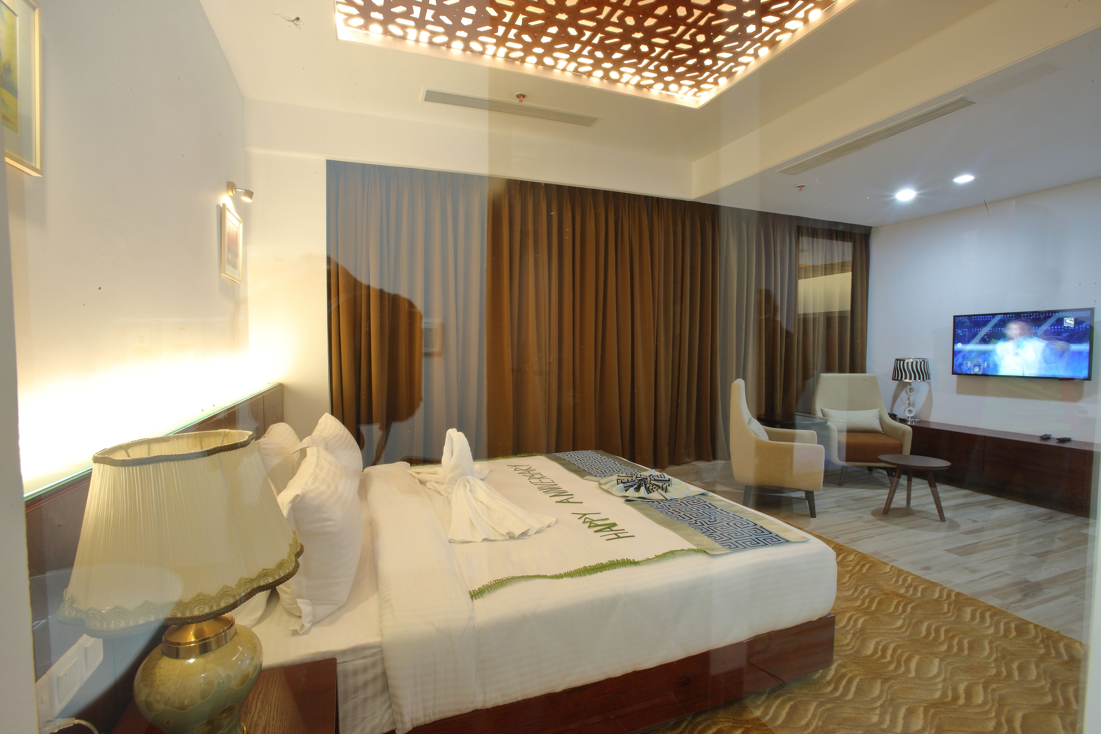 A hotel room with a neatly made bed, a television on the wall, and a seating area with a chair and a small table.
