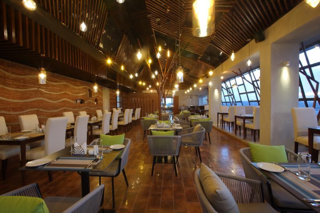 Un restaurante espacioso con techos altos, luces colgantes y vistas al mar a través de amplios ventanales.