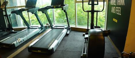Un gimnasio con cintas de correr, una bicicleta estática y un banco para pesas.