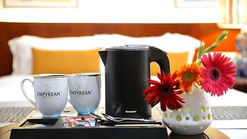 A hotel room with a bed, a tray table with two cups, a kettle, and a vase with flowers.
