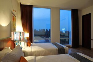 Habitación de hotel con dos camas, un ventanal grande y vistas a la ciudad.