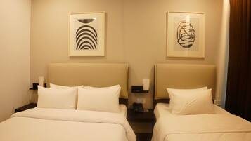 A hotel room with two beds, each with white bedding and headboards. There are framed abstract artworks on the walls above the beds.