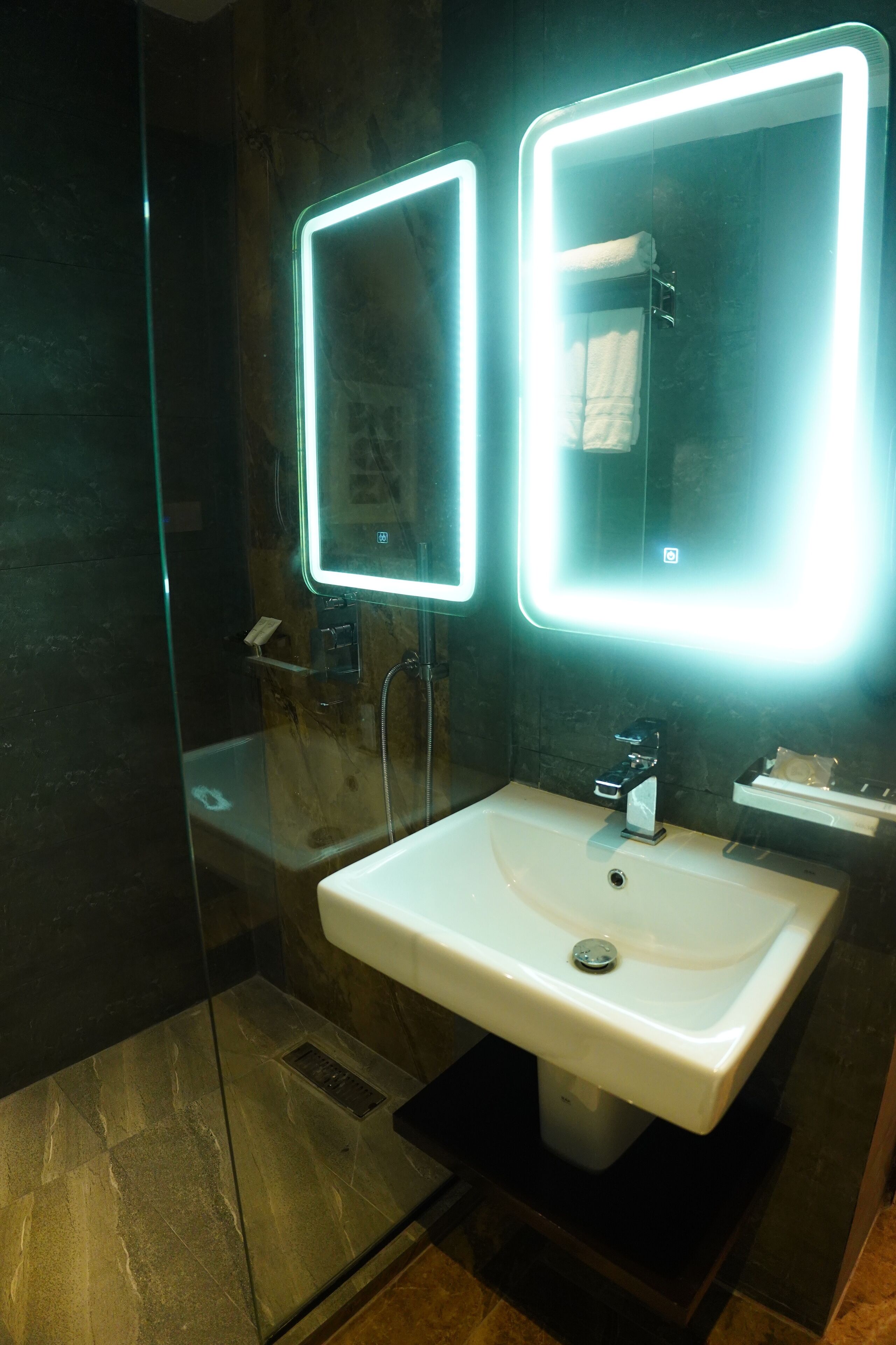A modern bathroom with a glass-enclosed shower, a white sink, and two illuminated mirrors.