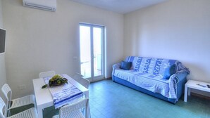 A room with a white table, two white chairs, a blue sofa with a patterned blanket, and a small white bench. - Appartamento Naia A: A graceful apartment located right on the beach, with Free WI-FI. (Sorrento)