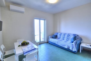 A room with a white table, two white chairs, a blue sofa with a patterned blanket, and a small white bench.
