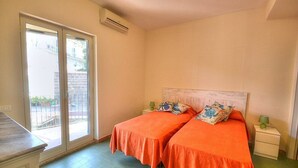 A bedroom with two beds, a sliding glass door to the outside, a small bedside table with a lamp, and an air conditioning unit on the wall. - Appartamento Naia A: A graceful apartment located right on the beach, with Free WI-FI. (Sorrento)