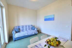 A room with a sofa against a wall, a dining table with chairs, and a fruit basket on the table.