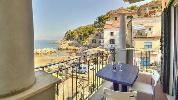 A balcony with a table and chairs overlooking a beach with buildings in the background. - Appartamento Naia A: A graceful apartment located right on the beach, with Free WI-FI. (Sorrento)