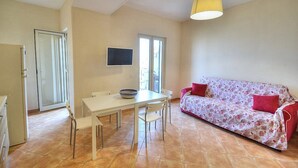 Un área de comedor con una mesa y sillas, un sofá y un televisor en la pared.