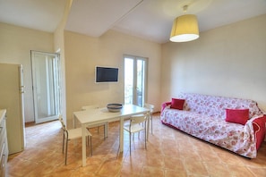 A dining area with a table and chairs, a sofa, and a television on the wall.