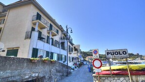 Una calle estrecha con edificios a un lado y un cielo azul despejado. Se ven indicaciones que dicen 'PUOLO' y una zona sin estacionamiento.