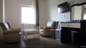A hotel room with two leather armchairs, a small table, a desk with a flat-screen TV, and a window with curtains. - Park Otel (Kayseri)