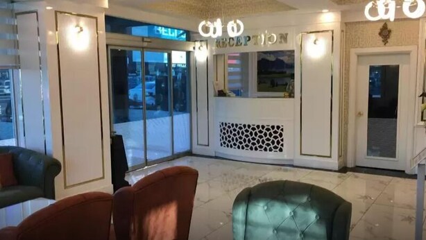 A reception area with a glass door entrance, a reception desk, and seating with a patterned wall. - Park Otel (Kayseri)