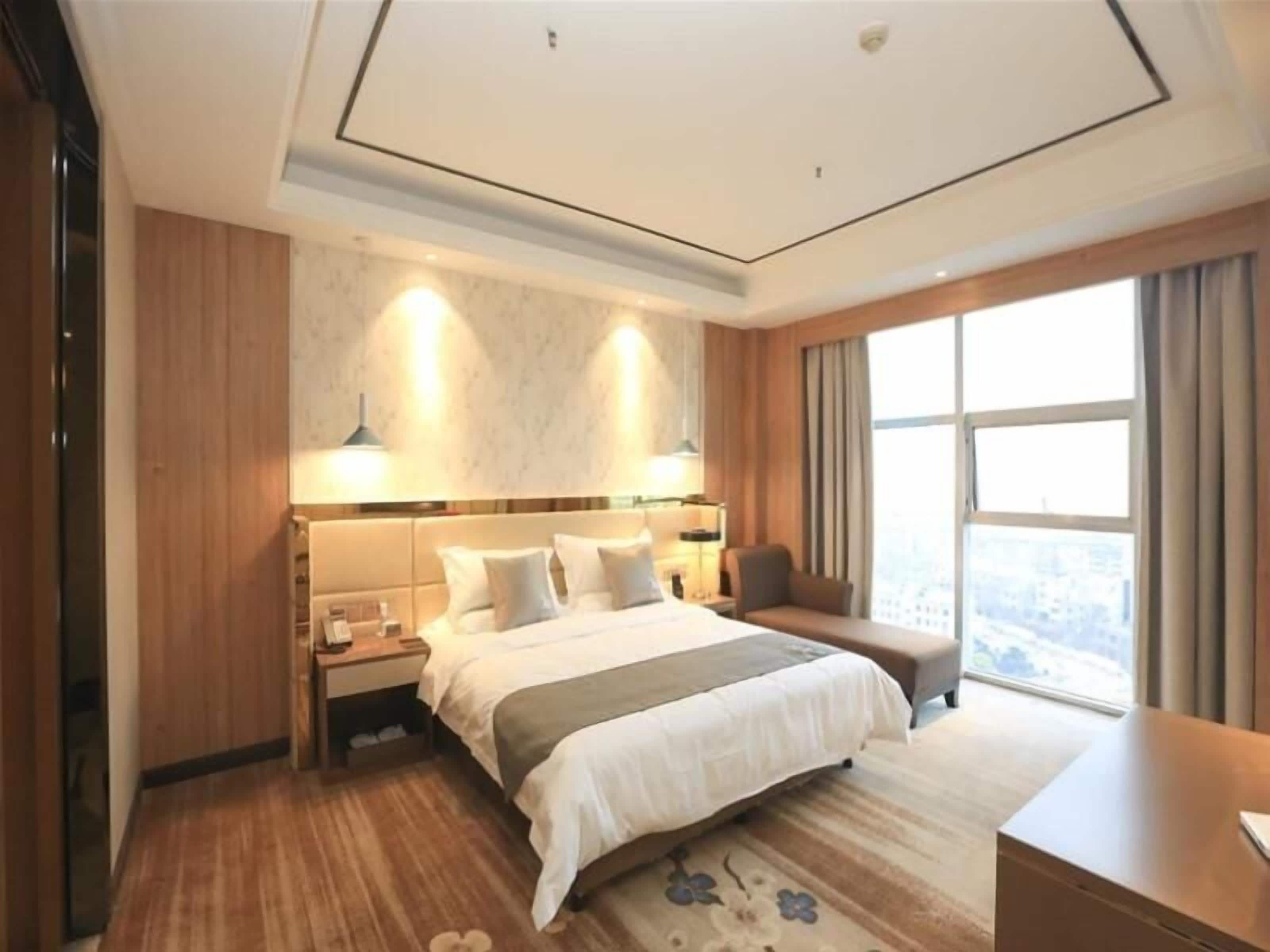 A hotel room with a large bed, a desk, a chair, and a window with a view.