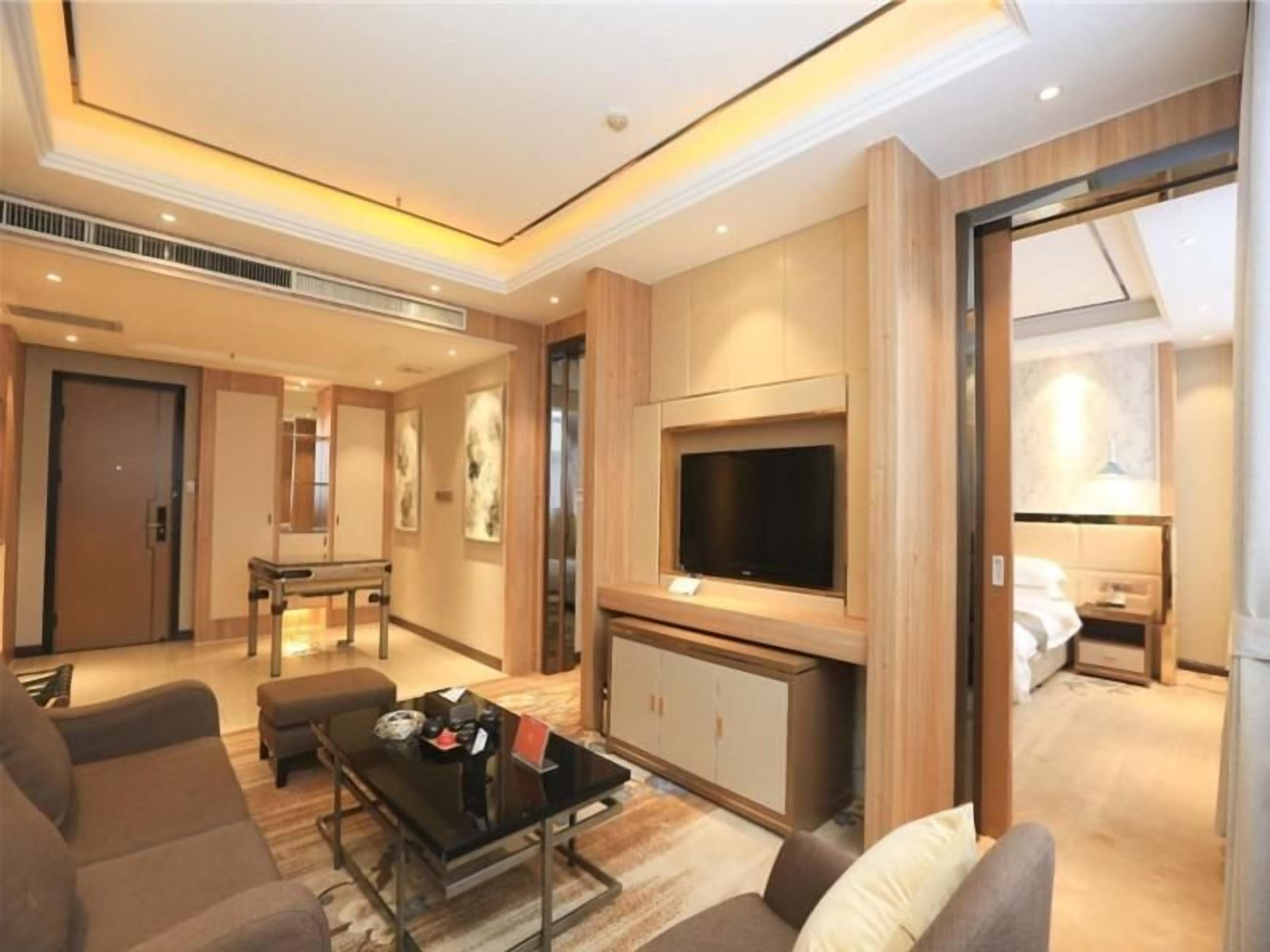 Una habitación de hotel moderna con televisión de pantalla plana, sofá, mesa de centro y zona de comedor con mesa y sillas.