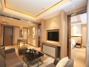 A modern hotel room with a flat-screen TV, a sofa, a coffee table, and a dining area with a table and chairs.