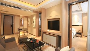 A modern hotel room with a flat-screen TV, a dining area with a table and chairs, and a cozy seating area with sofas and a coffee table.
