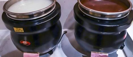 Dos recipientes negros con tapas metálicas, cada uno con una pequeña etiqueta y un asa dorada.