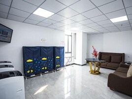 A modern office space with a clean, white interior, a brown sofa, a small round table, and a blue partition with yellow and blue patterns.