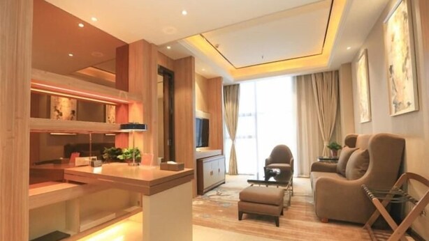 A modern living room with a sofa, a coffee table, and a TV. There is a kitchen area with a counter and cabinets.