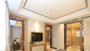A modern hotel room with a large bed, a flat-screen TV, a desk with a chair, and a bathroom visible through an open door.