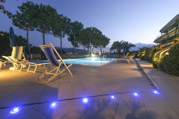 An outdoor pool area with lounge chairs and a view of the mountains at dusk.