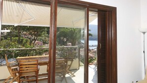 Un balcón con una mesa y sillas de madera, vistas a una zona costera con edificios y una extensión de agua.