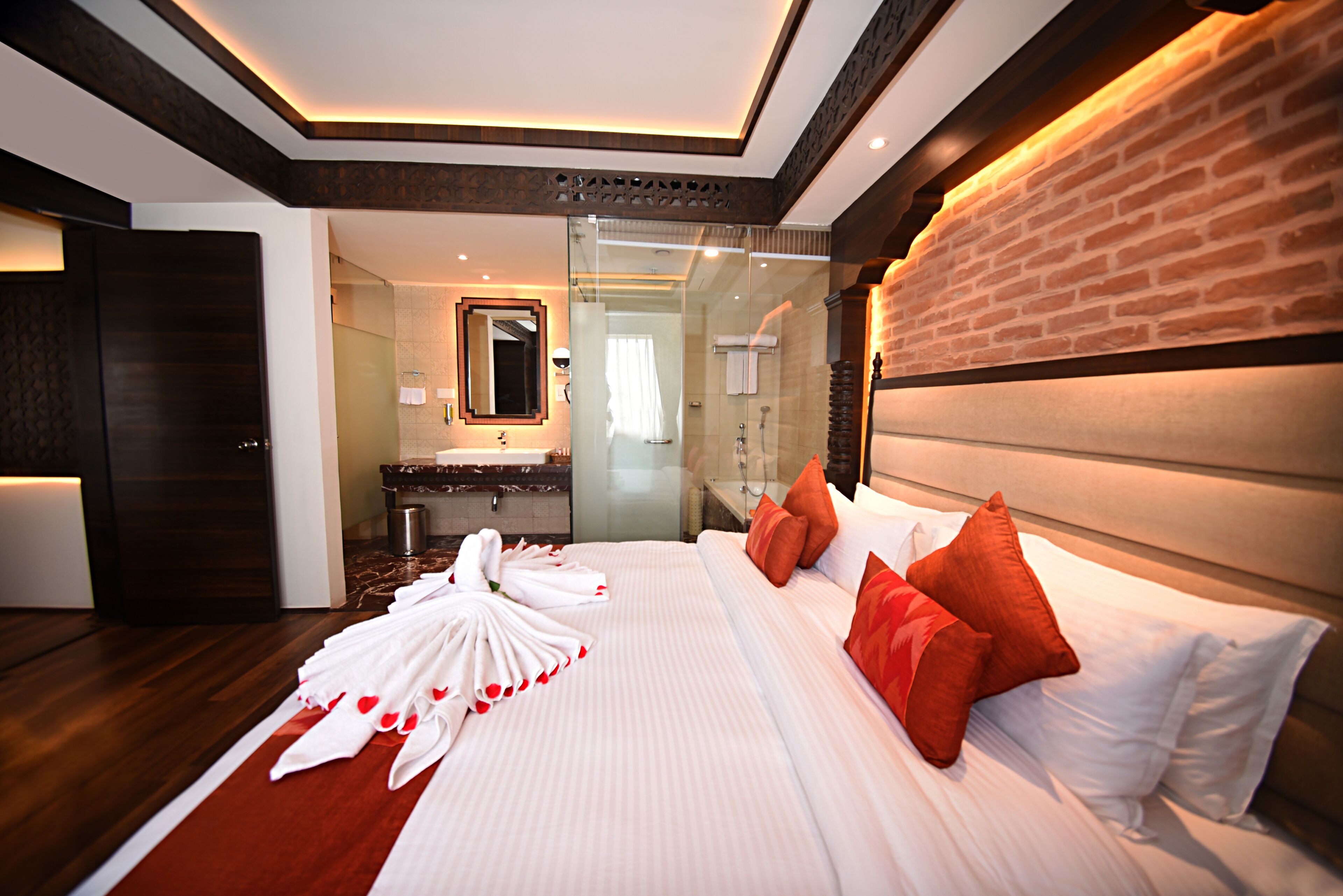 Habitación de hotel con una cama grande, cabina de ducha de vidrio, cabecera de madera y baño visible con lavamanos y espejo.