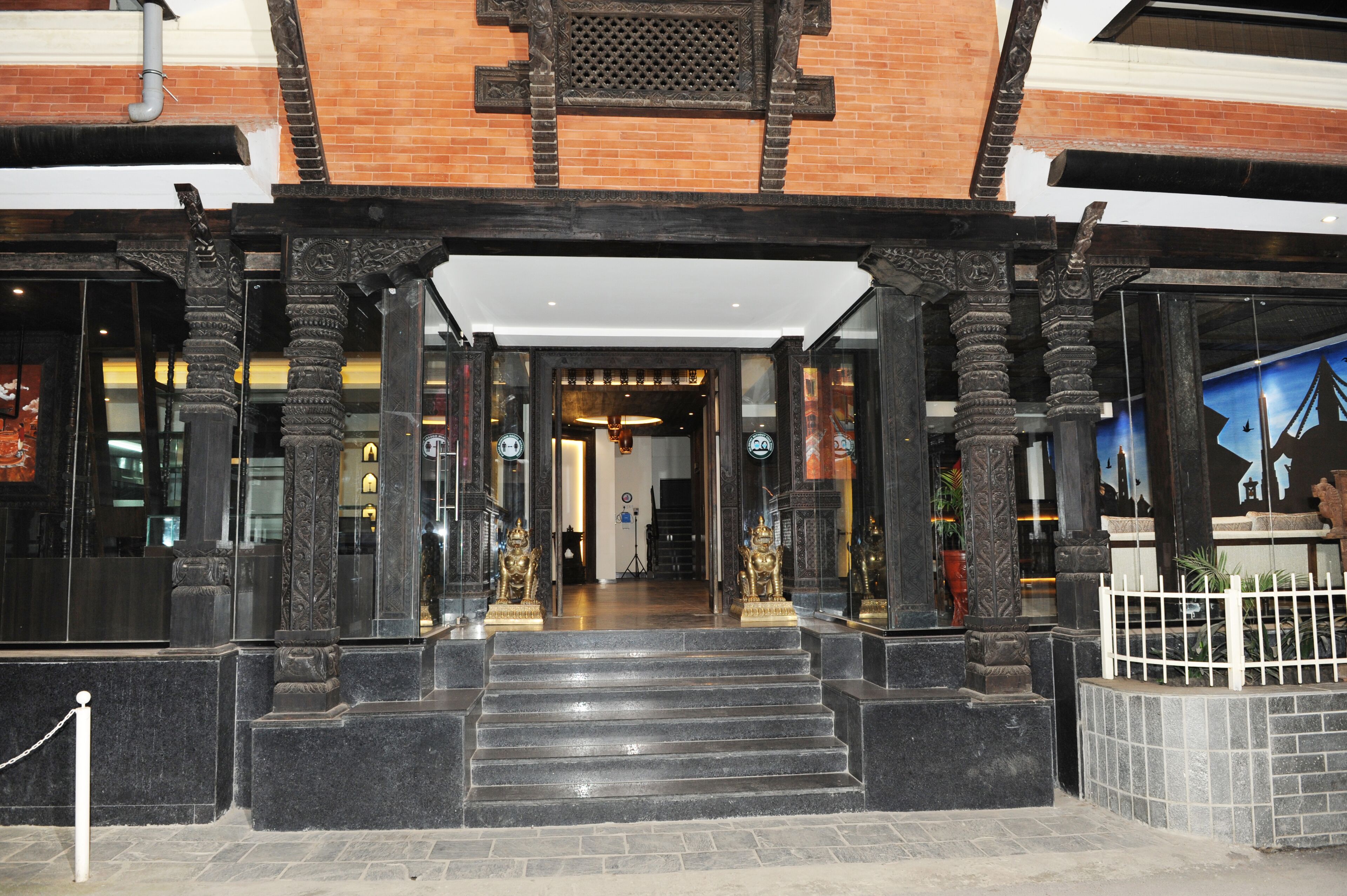 A building entrance with a brick facade, black columns, and a white fence.