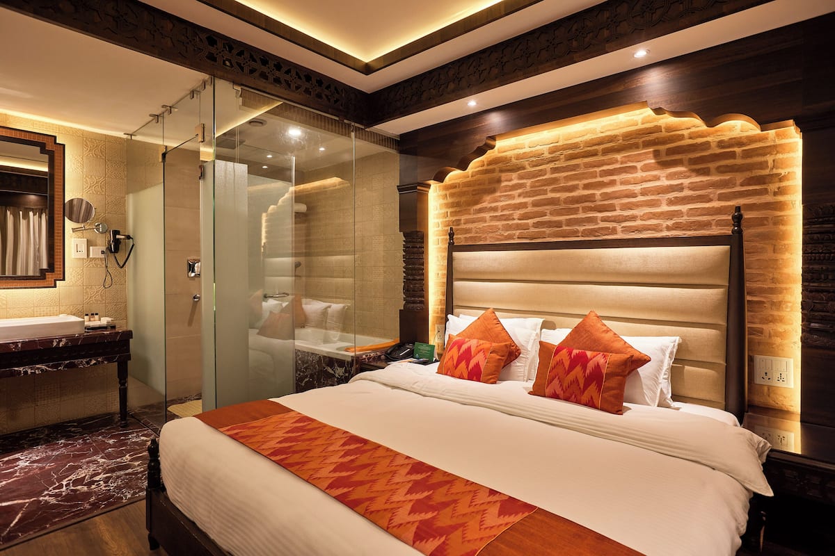 A hotel room with a large bed, a glass shower enclosure, a marble-topped vanity, and a brick-patterned headboard.
