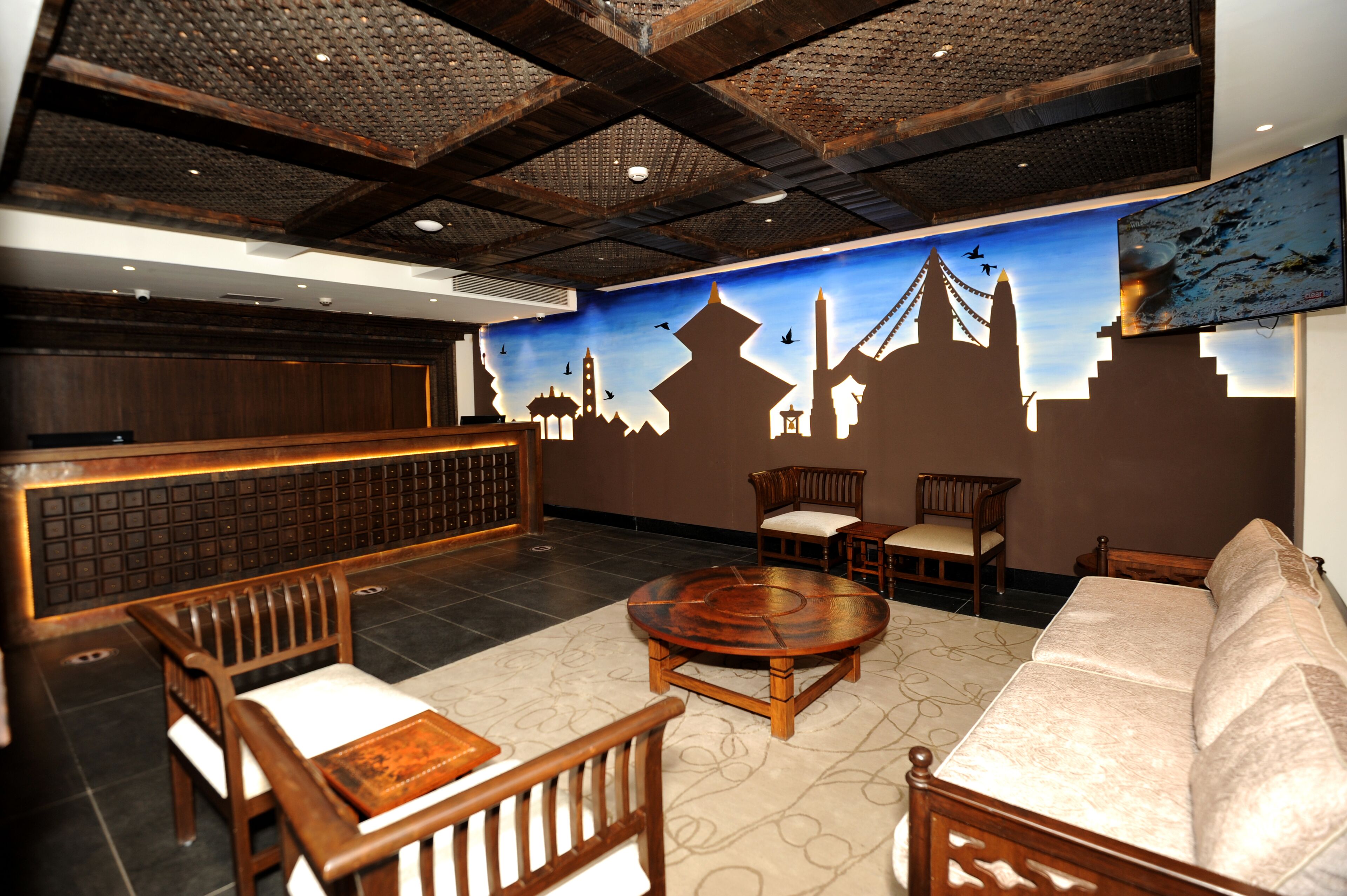 A lobby with a reception desk, wooden chairs, a sofa, and a round table.